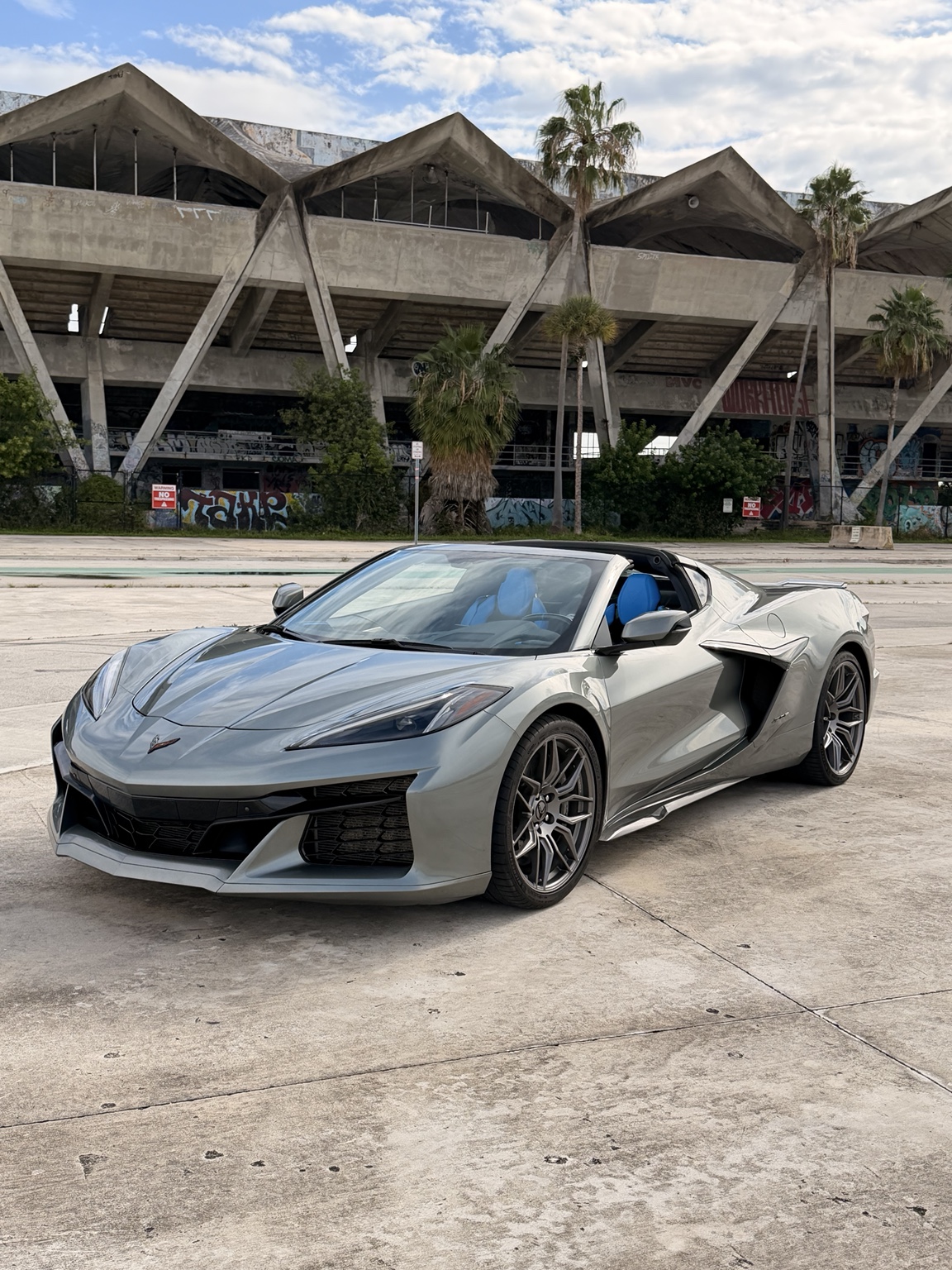 Gray Corvette Z06 with blue seats and the roof open in front of Miami Marine Stadium